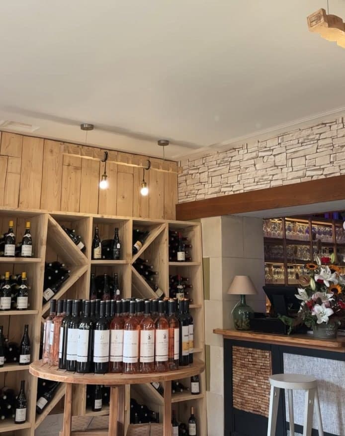 La cave : casiers en bois clair, table ronde de bouteilles et comptoir du bar au fond